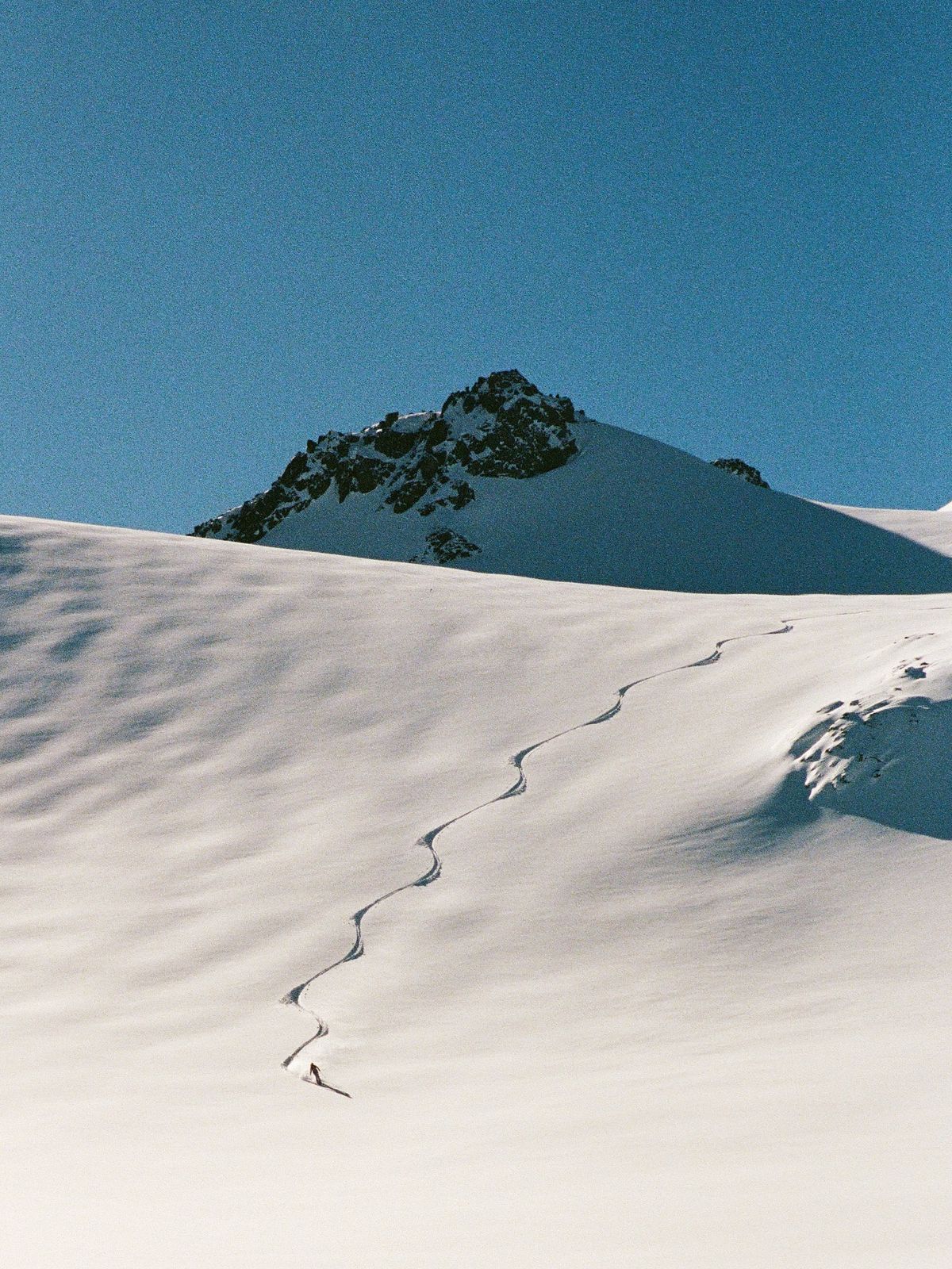 A skier tracing fresh tracks across an untouched snow-covered mountain